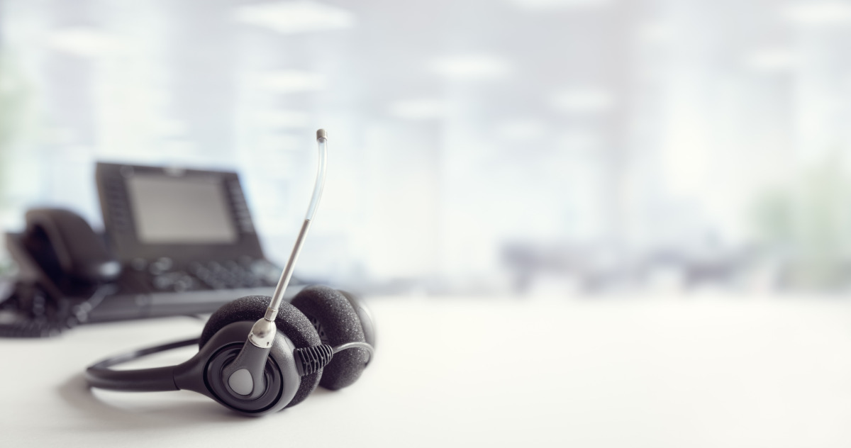 A VoIP headset resting on a desk with a phone blurred in the background