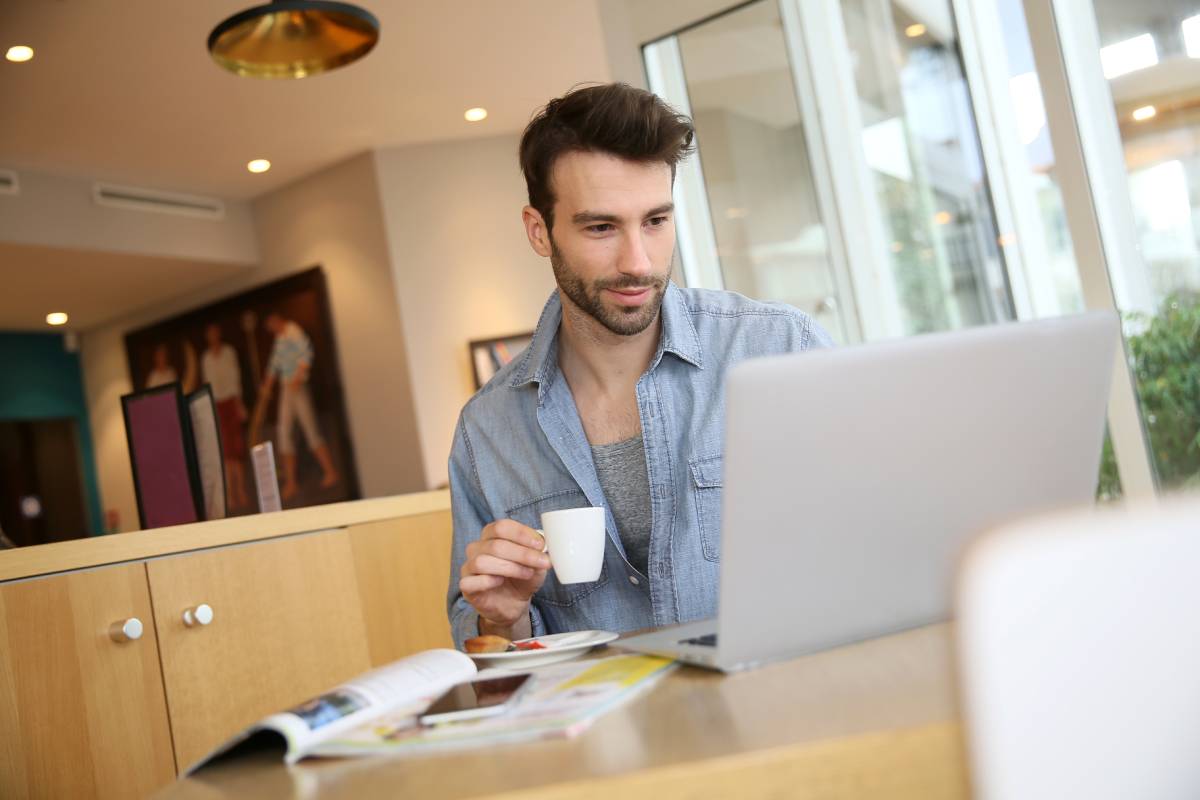 A man working from home using a laptop and drinking coffee