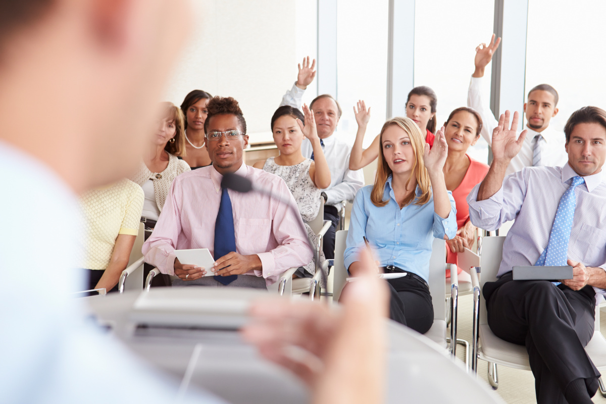 Group of People Seated before Speaker at a Business Conference with Their Hands Raised