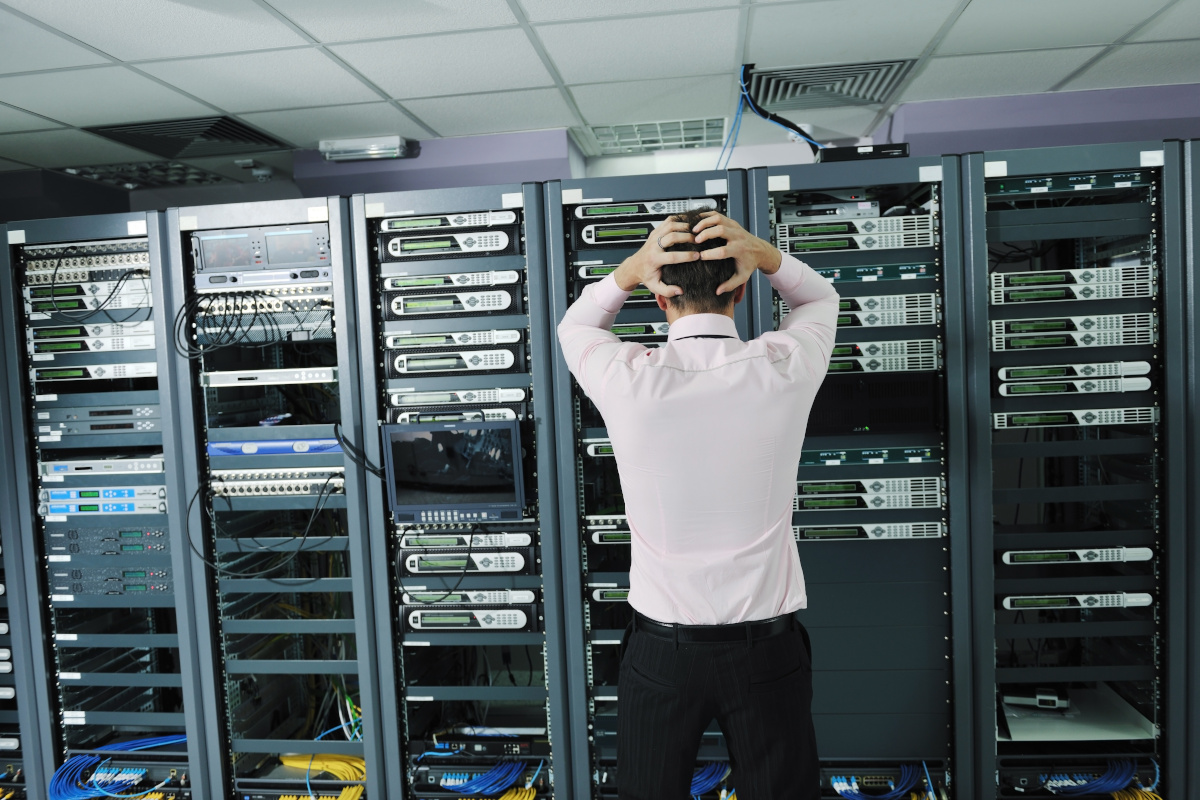 A person standing infront of server hardware with their hands on their head visibly distraught over issues with server data
