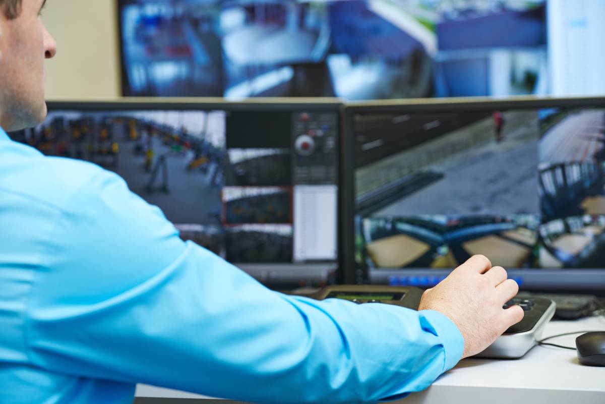 A man in a blue shirt reviewing security camera footage on three different screens