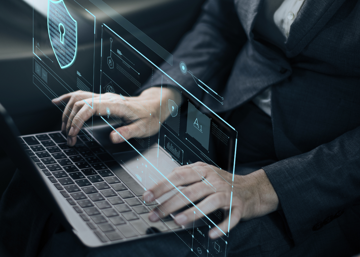  Close up of a man in a suit typing on a laptop with a holographic display with a shield that has a keyhole on it over his hands to represent cyber insurance