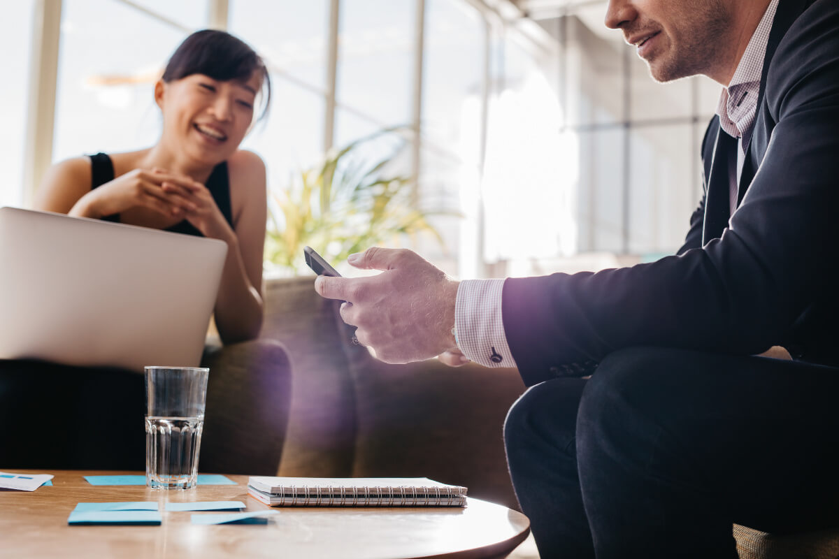 Smiling Business Man and Woman on Mobile Devices in Lobby Setting