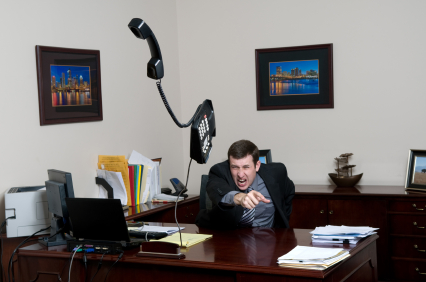 Businessman throwing a desktop phone across the room from behind an office desk