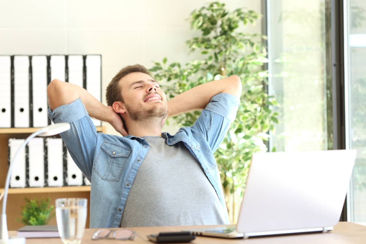 A man working remotely on his laptop and his hands behind his head