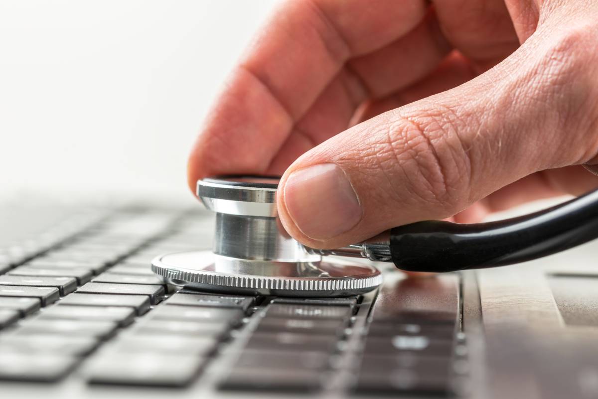 A man's hand holding a stethoscope to a keyboard