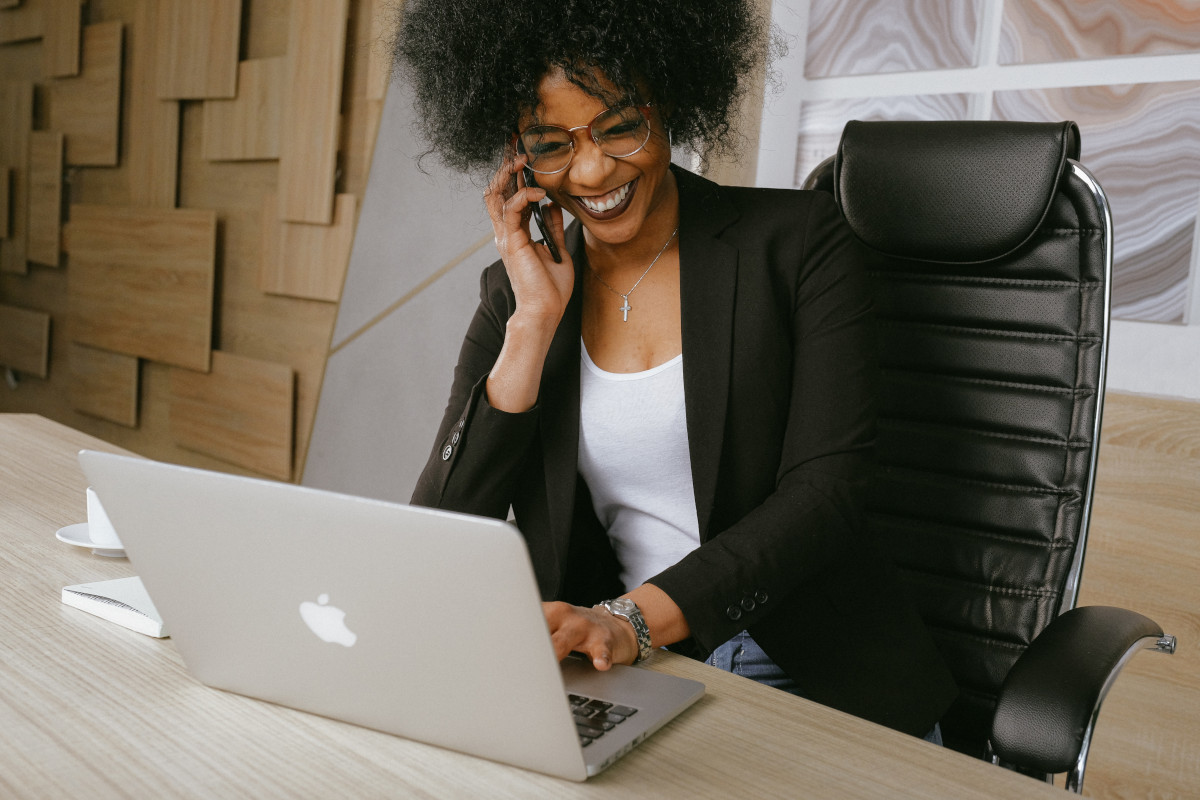 A woman in a black blazer sitting on a black office chair and talking on the phone